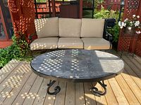 Front view of beige-cushioned metal sofa and oval stone-top coffee table