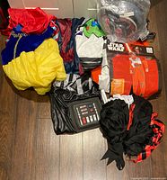 All costumes piled together with visible Snow White skirt, Buzz Lightyear chest, packaged Poe Dameron suit and accessory bag