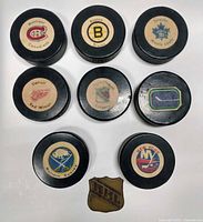 Group shot of eight team logo pucks and one metal NHL badge