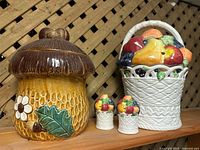 Fruit basket cookie jar, toadstool cookie jar, salt and pepper shakers together on shelf