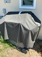 Grill fully covered with grey fabric cover against wall