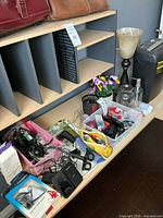 Overview of shelf with two leather bags, file sorter, organizers filled with office supplies, artificial flowers, lamp base, shredder