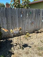 Overall view of fence area showing planter on stand, butterfly stake, additional stakes, and wall décor