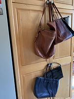 Four handbags hanging: two brown/tan, black tote, black patent clutch partially visible