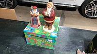 Two Santa figurines positioned on decorative Christmas box