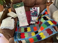 All linens displayed on chair: packaged Contessa towel set, burgundy and floral towels, crocheted throw, two stacks of napkins