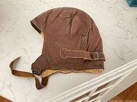 Left side view of brown leather flight helmet showing exterior shape and chin strap