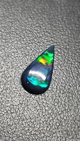 Pear-shaped Ethiopian black opal showing multicolor play-of-color on textured background