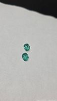 Two vivid green cushion-cut emeralds on white background