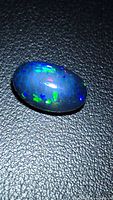 Oval black opal on dark background showing honeycomb pattern and colour play