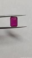 Front view of emerald-cut ruby held by tweezers