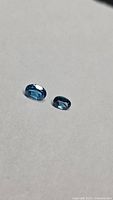 Two oval blue topaz gemstones on neutral background