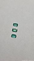 Three loose cushion-cut green emeralds laid vertically on neutral background