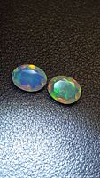 Pair of oval faceted opals on black background showing play-of-color