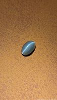 Oblique view of oval cabochon catseye alexandrite on textured background