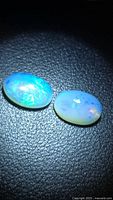 Two oval Ethiopian crystal opals on black textured surface showing blue-green play-of-color
