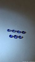 Seven oval faceted violet-blue tanzanites on neutral background