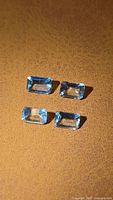 Four emerald-cut aquamarine gemstones on textured background
