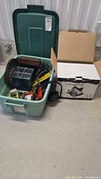 Closed view of green tote filled with assorted hand tools next to boxed Altocraft circular saw