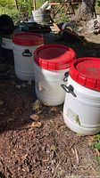 Three white plastic drums with red lids placed outdoors