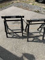 Two folding adjustable steel sawhorses standing on pavement