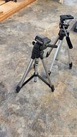 Two aluminum camera tripods standing on floor