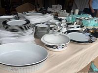 Wide view of stacked plates, bowls, cups, flatware and serving pieces