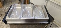 Front view showing three stainless trays with clear lids in warming base