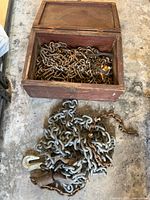 Overview of wood box full of rusty chains and separate galvanized chain with hook