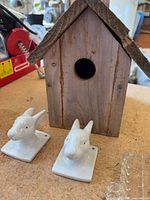 Wooden birdhouse front with two ceramic rabbit head hooks and edge of glass tray visible