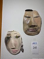 Both clay face masks hanging on wall showing relative size and features