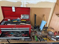 Overall view of red toolbox on bench with surrounding axe, wedge, hammers and additional tools