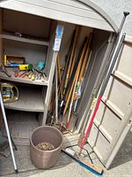 Plastic shed exterior, planter, broom, long-handled tools visible