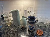 Group shot of all seven vases and two flower frogs on countertop