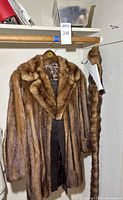 Full view of brown fur coat hanging, belt visible, additional fur piece hanging beside