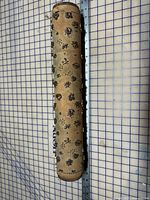 Full view of wallpaper roller showing wood body, metal floral pattern and size reference grid/ruler