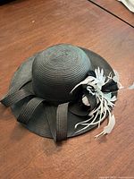 Top view of black derby hat with ribbon loops and feather accent