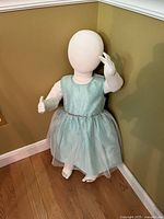 Full view of fabric child mannequin wearing dress standing against wall