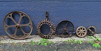 Front view of five cast metal gears of various sizes lined up against wall