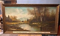 Full view of framed river and mountain landscape oil painting with ruler for scale