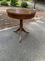 Full view of round wooden pedestal table showing top, column and tripod base