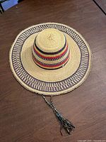 Top view of woven straw sombrero style hat showing crown stripes, brim pattern and braided tassel cord