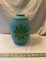 Full view of turquoise glass cookie jar with daisy graphic beside ruler