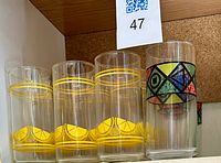 Row of clear highball glasses; majority with yellow lemon band, one with multicolor geometric band visible