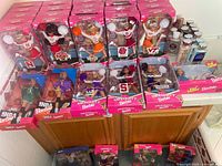 Group shot of approximately 20 boxed dolls on countertop – University and NBA series visible