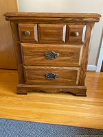 Front view of solid wood bedside table showing three drawers and hardware