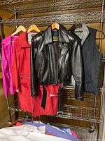Rack with four outerwear items: pink windbreaker, red coat, black leather jacket, reversible vest