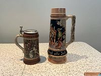 Both steins front view showing size difference and relief artwork