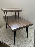 Angled view showing two-tier design, walnut laminate top, black tapered legs with brass tips