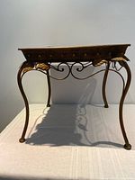 Full side view of metal table showing legs and decorative scrolls